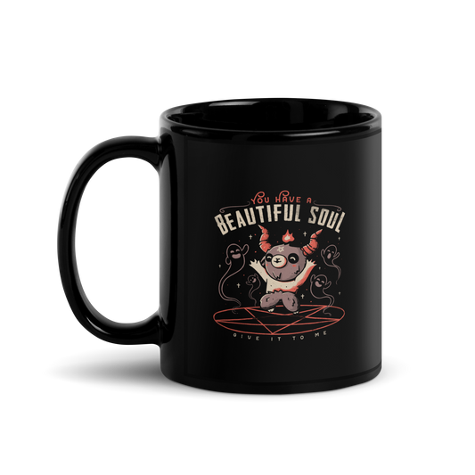 This design features a cute, cartoonish character with horns and a pentagram on its forehead, standing on a red circle with ghost-like figures surrounding it. Above the character, the text reads 'You have a beautiful soul,' and below, 'Give it to me.' The design contrasts dark and cute imagery with playful lettering.