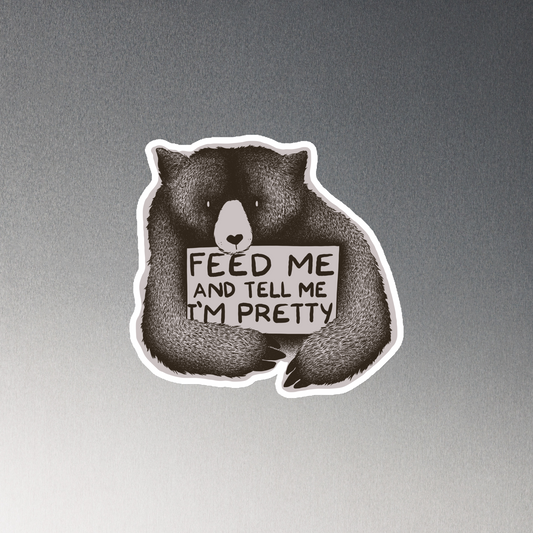 This drawing is of a cute, cartoon-style bear holding a sign with a heart-shaped nose and simple, expressive eyes. The sign reads, 'Feed me and tell me I'm pretty' in a handwritten, playful font. The bear's fur is detailed with fine, textured lines, giving it a cozy, endearing look. The drawing has a monochrome, black-and-white color scheme