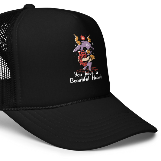 The design features a cute, cartoonish, anthropomorphic goat with big horns and a flame above its head, standing on a red pentagram. The goat has a star on its forehead and is hugging a large, anatomically correct human heart. The text below reads, 'You have a Beautiful Heart'. The image combines elements of occult symbolism with a playful, endearing aesthetic.