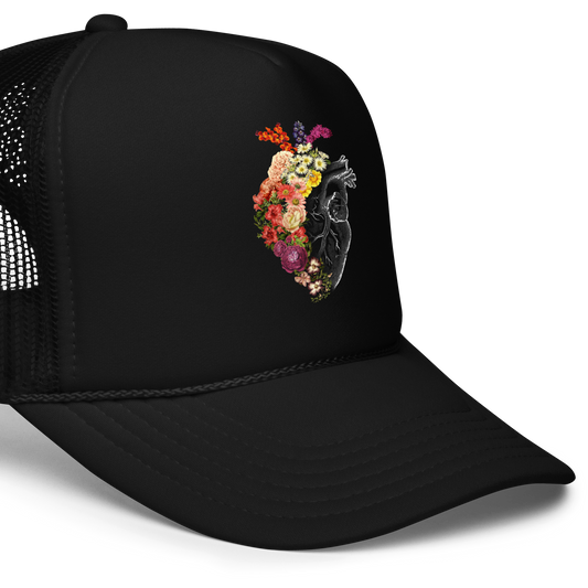 The design is an intricate and anatomical drawing of a human heart on a black background. The left side of the heart morphs into a vibrant assortment of colorful flowers, including roses, daisies, and other blooming blossoms, creating a striking contrast between the realistic and the surreal, symbolizing the harmony between nature and humanity.