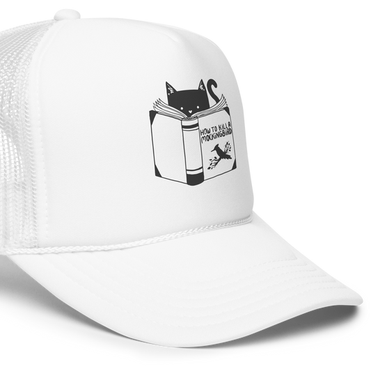 A black and white illustration features a cat peeking over an open book titled 'How to Kill a Mockingbird,' playfully altering the classic novel's title. The cat has a heart-shaped nose and simple, cute facial features. The design is whimsical and ironic, combining classic literature with a humorous twist.