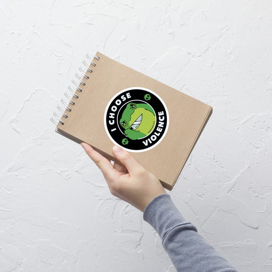 A charming, cartoon-style green frog holds a knife in its hand with a playful yet fierce expression. Encircled by bold text, 'I CHOOSE VIOLENCE,' the design mixes humor with an edge. Two small skulls flank the frog, adding a quirky, rebellious touch to the image. The overall effect balances cuteness and irony in a memorable way.