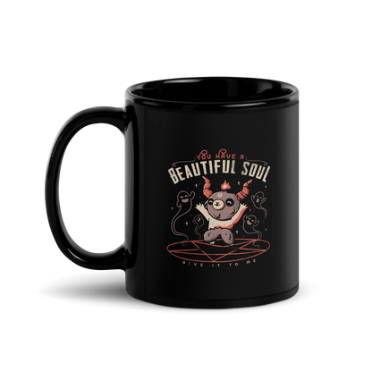 This design features a cute, cartoonish character with horns and a pentagram on its forehead, standing on a red circle with ghost-like figures surrounding it. Above the character, the text reads 'You have a beautiful soul,' and below, 'Give it to me.' The design contrasts dark and cute imagery with playful lettering.