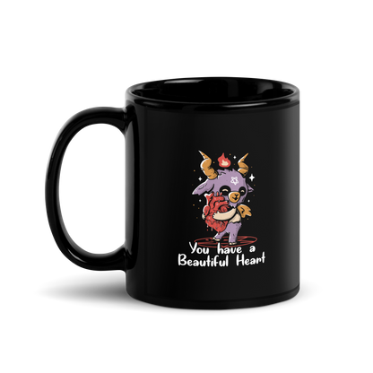 The design features a cute, cartoonish, anthropomorphic goat with big horns and a flame above its head, standing on a red pentagram. The goat has a star on its forehead and is hugging a large, anatomically correct human heart. The text below reads, 'You have a Beautiful Heart'. The image combines elements of occult symbolism with a playful, endearing aesthetic.