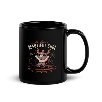 This design features a cute, cartoonish character with horns and a pentagram on its forehead, standing on a red circle with ghost-like figures surrounding it. Above the character, the text reads 'You have a beautiful soul,' and below, 'Give it to me.' The design contrasts dark and cute imagery with playful lettering.