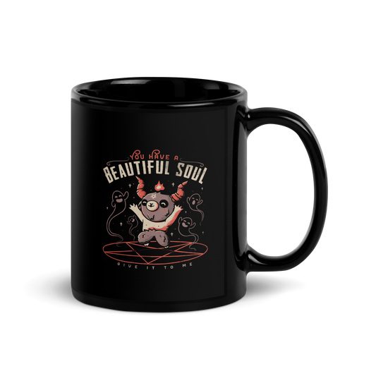 This design features a cute, cartoonish character with horns and a pentagram on its forehead, standing on a red circle with ghost-like figures surrounding it. Above the character, the text reads 'You have a beautiful soul,' and below, 'Give it to me.' The design contrasts dark and cute imagery with playful lettering.