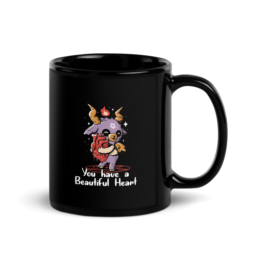 The design features a cute, cartoonish, anthropomorphic goat with big horns and a flame above its head, standing on a red pentagram. The goat has a star on its forehead and is hugging a large, anatomically correct human heart. The text below reads, 'You have a Beautiful Heart'. The image combines elements of occult symbolism with a playful, endearing aesthetic.