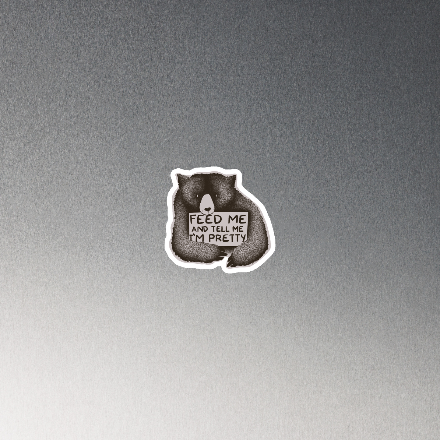 This drawing is of a cute, cartoon-style bear holding a sign with a heart-shaped nose and simple, expressive eyes. The sign reads, 'Feed me and tell me I'm pretty' in a handwritten, playful font. The bear's fur is detailed with fine, textured lines, giving it a cozy, endearing look. The drawing has a monochrome, black-and-white color scheme