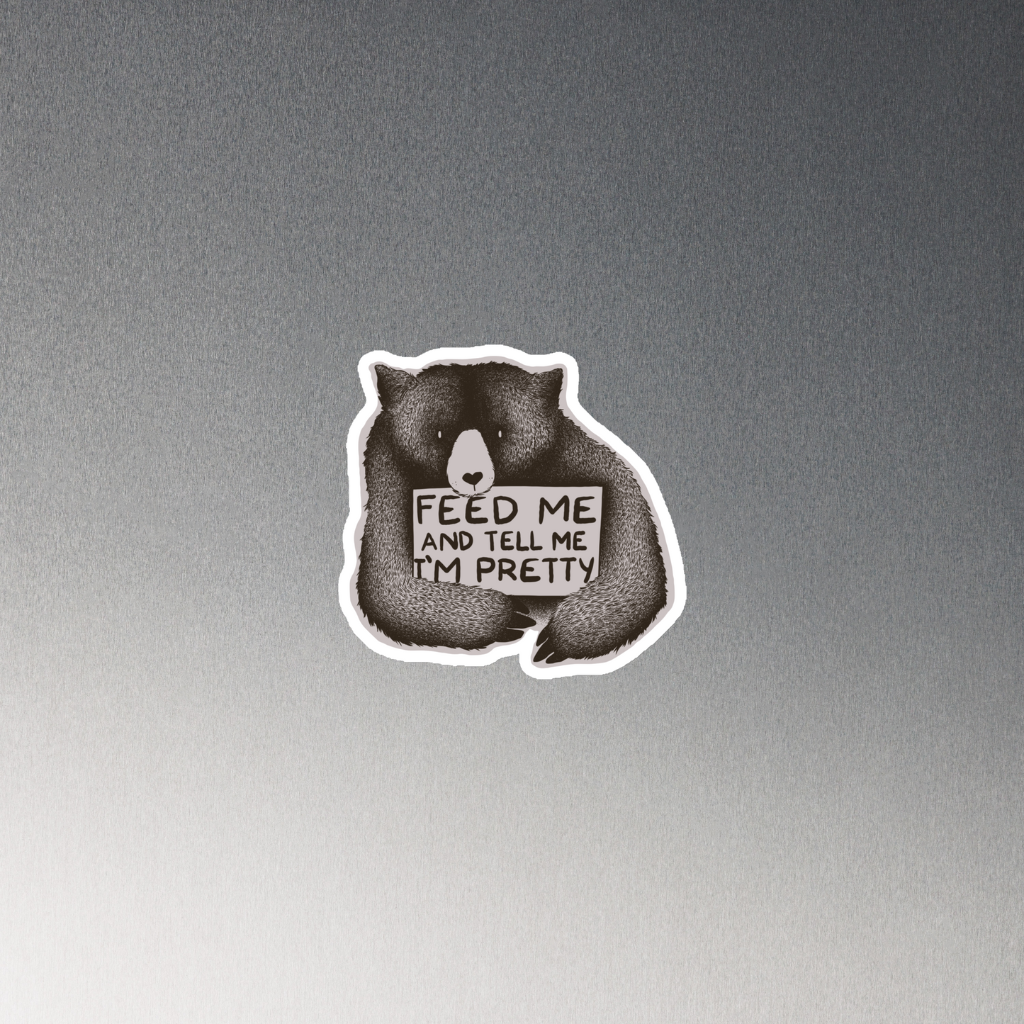 This drawing is of a cute, cartoon-style bear holding a sign with a heart-shaped nose and simple, expressive eyes. The sign reads, 'Feed me and tell me I'm pretty' in a handwritten, playful font. The bear's fur is detailed with fine, textured lines, giving it a cozy, endearing look. The drawing has a monochrome, black-and-white color scheme