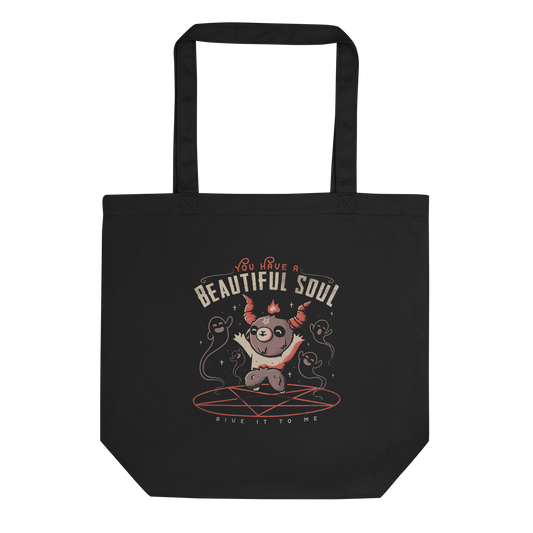 This design features a cute, cartoonish character with horns and a pentagram on its forehead, standing on a red circle with ghost-like figures surrounding it. Above the character, the text reads 'You have a beautiful soul,' and below, 'Give it to me.' The design contrasts dark and cute imagery with playful lettering.