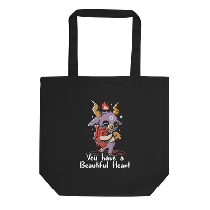 The design features a cute, cartoonish, anthropomorphic goat with big horns and a flame above its head, standing on a red pentagram. The goat has a star on its forehead and is hugging a large, anatomically correct human heart. The text below reads, 'You have a Beautiful Heart'. The image combines elements of occult symbolism with a playful, endearing aesthetic.