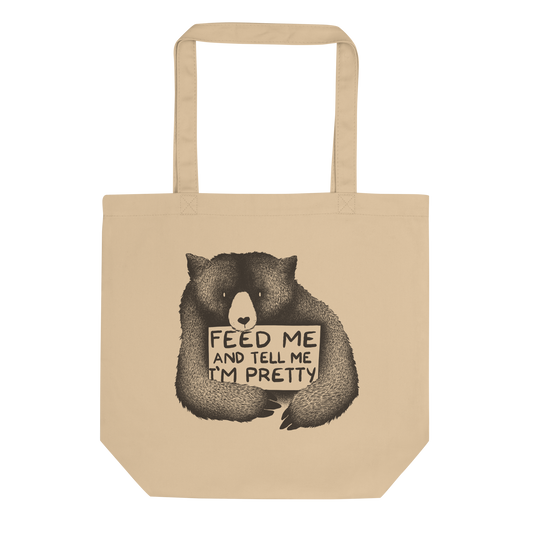This drawing is of a cute, cartoon-style bear holding a sign with a heart-shaped nose and simple, expressive eyes. The sign reads, 'Feed me and tell me I'm pretty' in a handwritten, playful font. The bear's fur is detailed with fine, textured lines, giving it a cozy, endearing look. The drawing has a monochrome, black-and-white color scheme