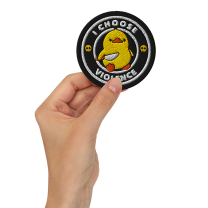The image displays a cute, cartoon-style yellow duck character holding a knife with a determined expression. The duck is centered inside a circular design with the text 'I CHOOSE FIGHT' around it. Two small skulls flanking the duck add a humorous, combative touch to the design.