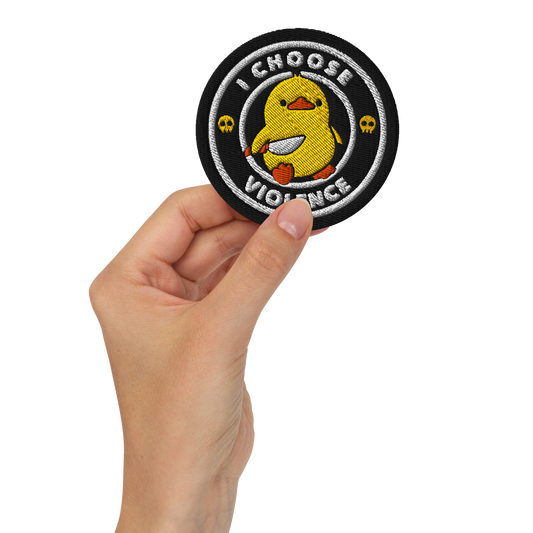 The image displays a cute, cartoon-style yellow duck character holding a knife with a determined expression. The duck is centered inside a circular design with the text 'I CHOOSE FIGHT' around it. Two small skulls flanking the duck add a humorous, combative touch to the design.