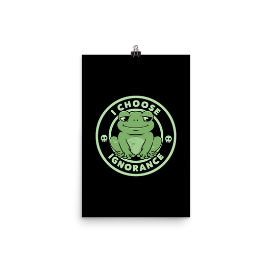 The image shows a cartoonish green frog with a sly smile, sitting with legs splayed out. Around it, the phrase 'I CHOOSE IGNORANCE' is written in bold letters. Two small skull designs are included, one on each side of the frog. The style is playful and ironic, blending elements of humor and rebellion.