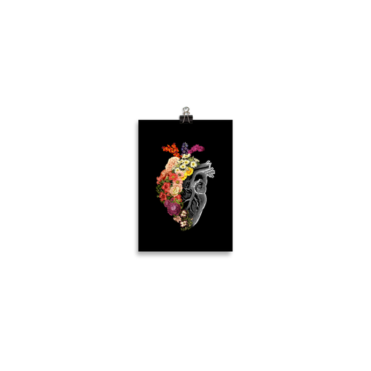 The design is an intricate and anatomical drawing of a human heart on a black background. The left side of the heart morphs into a vibrant assortment of colorful flowers, including roses, daisies, and other blooming blossoms, creating a striking contrast between the realistic and the surreal, symbolizing the harmony between nature and humanity.