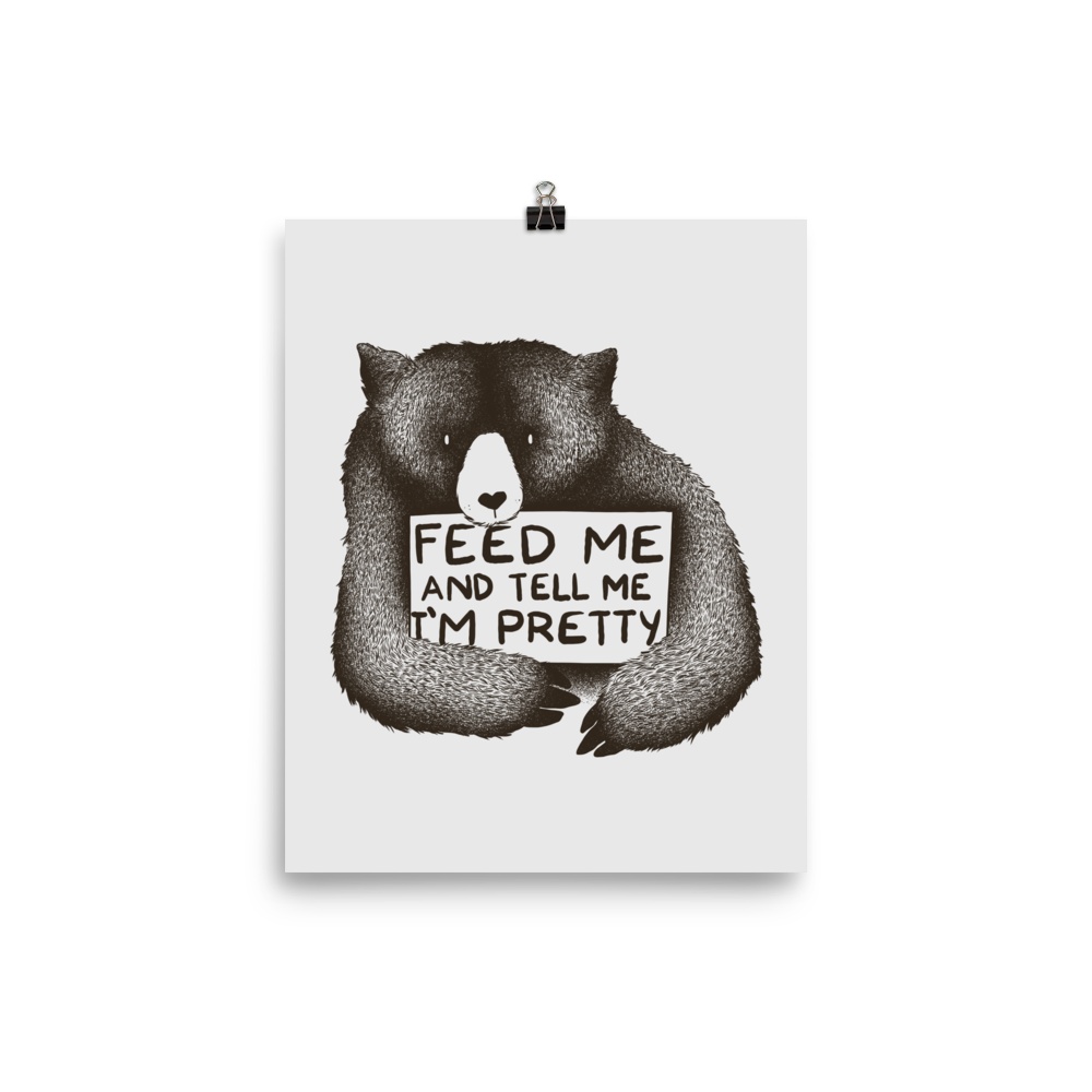 This drawing is of a cute, cartoon-style bear holding a sign with a heart-shaped nose and simple, expressive eyes. The sign reads, 'Feed me and tell me I'm pretty' in a handwritten, playful font. The bear's fur is detailed with fine, textured lines, giving it a cozy, endearing look. The drawing has a monochrome, black-and-white color scheme