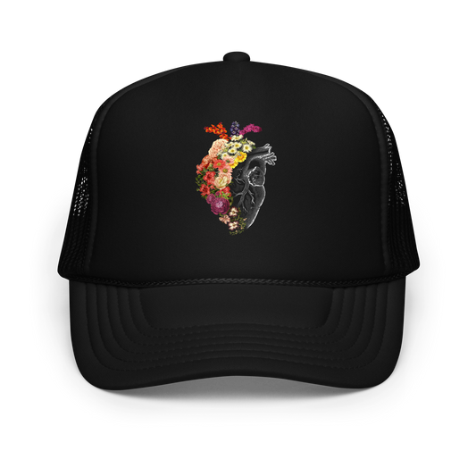 The design is an intricate and anatomical drawing of a human heart on a black background. The left side of the heart morphs into a vibrant assortment of colorful flowers, including roses, daisies, and other blooming blossoms, creating a striking contrast between the realistic and the surreal, symbolizing the harmony between nature and humanity.