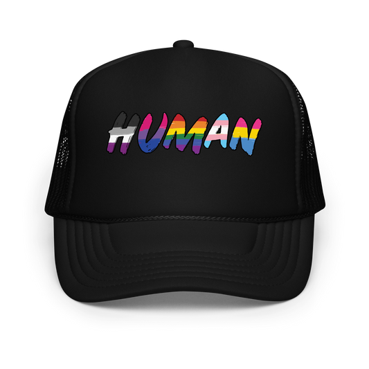 The image displays the word 'HUMAN' in bold, capitalized letters filled with colorful pride flag patterns. The colors within the letters represent different LGBTQ+ pride flags, symbolizing inclusivity and diversity. The background is solid black, which makes the colorful patterns stand out more vibrantly.