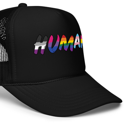 The image displays the word 'HUMAN' in bold, capitalized letters filled with colorful pride flag patterns. The colors within the letters represent different LGBTQ+ pride flags, symbolizing inclusivity and diversity. The background is solid black, which makes the colorful patterns stand out more vibrantly.