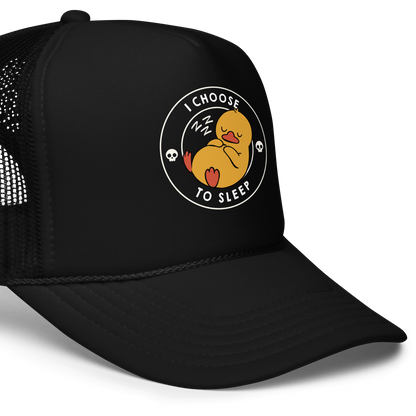 A cute, cartoonish yellow duck is peacefully sleeping with a contented expression. Its webbed feet and wings are tucked in. Around it, the words 'I Choose to Sleep' are inscribed in white letters. Two small skulls accompany this text, adding a humorous, edgy touch. The design is simple, charming, and playful, appealing to fans of ironic, whimsical art.