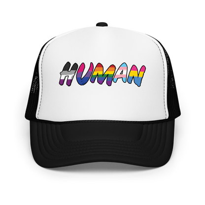 The image displays the word 'HUMAN' in bold, capitalized letters filled with colorful pride flag patterns. The colors within the letters represent different LGBTQ+ pride flags, symbolizing inclusivity and diversity. The background is solid black, which makes the colorful patterns stand out more vibrantly.