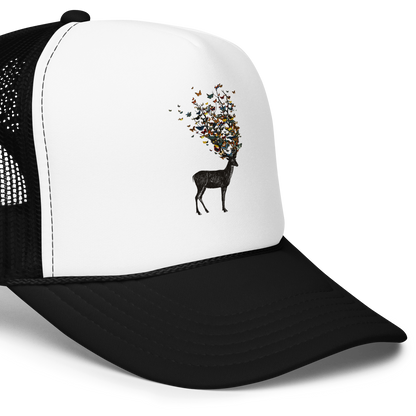 The image depicts a dark, silhouetted deer standing on a neutral background. Instead of branches, its antlers transform into a swirling cloud of vibrant, colorful butterflies that extend upwards and outward. The mix of organic and ethereal elements creates a captivating and whimsical visual contrast.