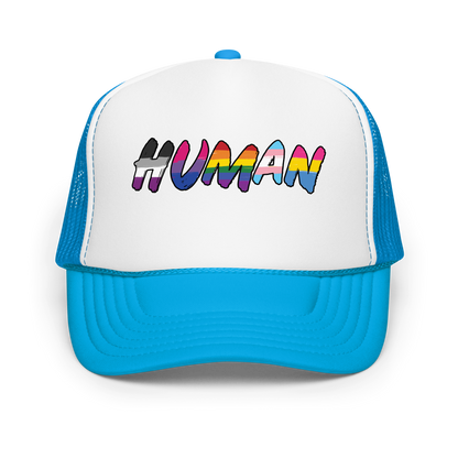 The image displays the word 'HUMAN' in bold, capitalized letters filled with colorful pride flag patterns. The colors within the letters represent different LGBTQ+ pride flags, symbolizing inclusivity and diversity. The background is solid black, which makes the colorful patterns stand out more vibrantly.