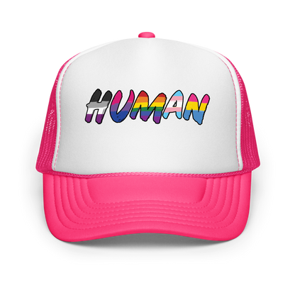 The image displays the word 'HUMAN' in bold, capitalized letters filled with colorful pride flag patterns. The colors within the letters represent different LGBTQ+ pride flags, symbolizing inclusivity and diversity. The background is solid black, which makes the colorful patterns stand out more vibrantly.