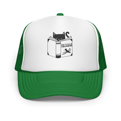 A black and white illustration features a cat peeking over an open book titled 'How to Kill a Mockingbird,' playfully altering the classic novel's title. The cat has a heart-shaped nose and simple, cute facial features. The design is whimsical and ironic, combining classic literature with a humorous twist.