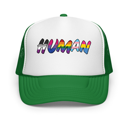 The image displays the word 'HUMAN' in bold, capitalized letters filled with colorful pride flag patterns. The colors within the letters represent different LGBTQ+ pride flags, symbolizing inclusivity and diversity. The background is solid black, which makes the colorful patterns stand out more vibrantly.