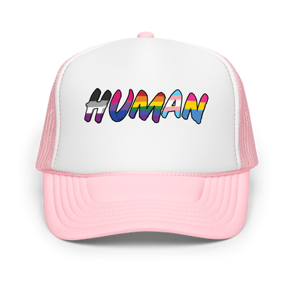 The image displays the word 'HUMAN' in bold, capitalized letters filled with colorful pride flag patterns. The colors within the letters represent different LGBTQ+ pride flags, symbolizing inclusivity and diversity. The background is solid black, which makes the colorful patterns stand out more vibrantly.