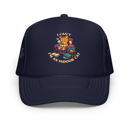 This cozy design features a contented orange cat sipping coffee in a comfy chair, surrounded by books and plants. The following message encircles the design: I CAN'T I'M AN INDOOR CAT.