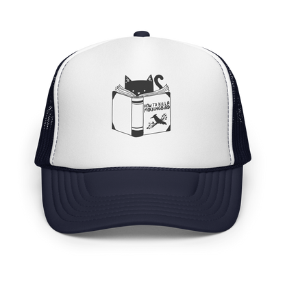 A black and white illustration features a cat peeking over an open book titled 'How to Kill a Mockingbird,' playfully altering the classic novel's title. The cat has a heart-shaped nose and simple, cute facial features. The design is whimsical and ironic, combining classic literature with a humorous twist.