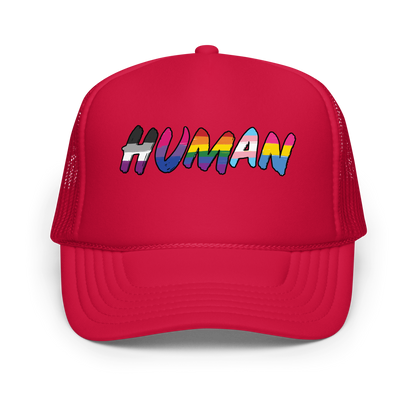 The image displays the word 'HUMAN' in bold, capitalized letters filled with colorful pride flag patterns. The colors within the letters represent different LGBTQ+ pride flags, symbolizing inclusivity and diversity. The background is solid black, which makes the colorful patterns stand out more vibrantly.