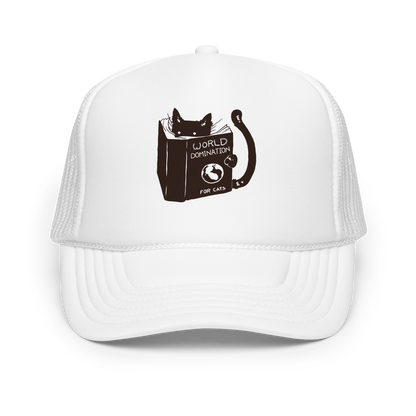 The design features a black silhouette of a cat peeking from behind an oversized book. The book's cover reads 'World Domination for Cats,' and includes a simple drawing of a globe. The cat's eyes are wide open, suggesting either surprise or intense focus on its 'world domination' plans.