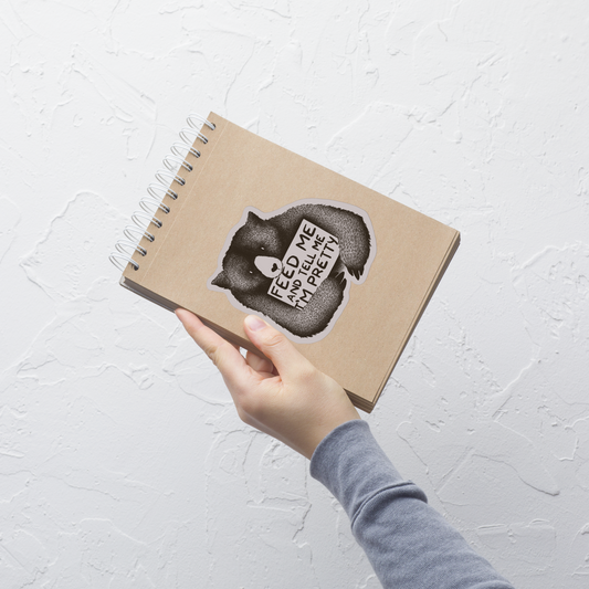 This drawing is of a cute, cartoon-style bear holding a sign with a heart-shaped nose and simple, expressive eyes. The sign reads, 'Feed me and tell me I'm pretty' in a handwritten, playful font. The bear's fur is detailed with fine, textured lines, giving it a cozy, endearing look. The drawing has a monochrome, black-and-white color scheme