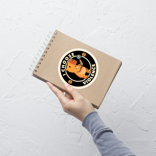 A cute, cartoonish burnt yellow capybara stands holding a spiked mace with a determined expression. Surrounding it is a circular design with the text 'I CHOOSE VIOLENCE' and two small skulls on either side, giving it a humorous yet ironic tone.