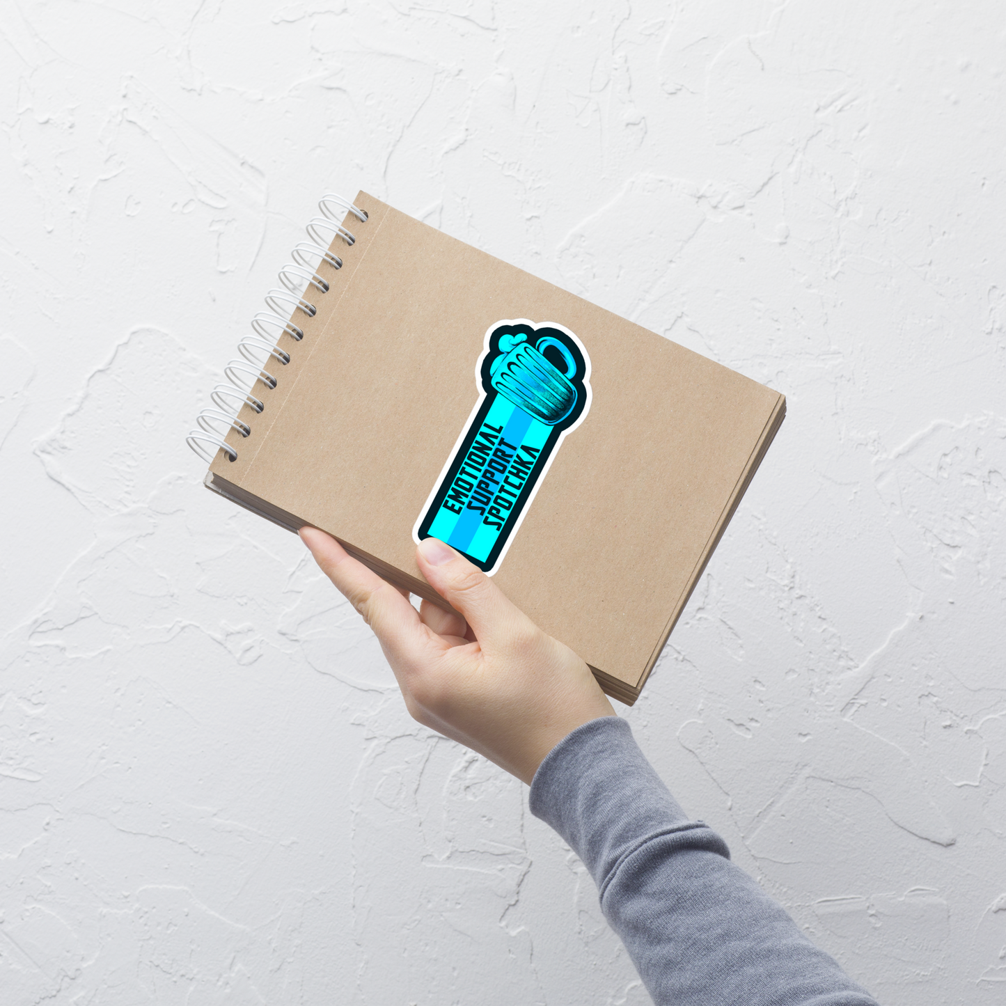 The design features a stylized mug filled with a frothy beverage, colored in vibrant shades of blue. Next to the mug, bold text reads 'EMOTIONAL SUPPORT SPOTCHKA'. The use of color and font style gives it a playful, pop-culture vibe, hinting at something fantastical or sci-fi influenced.