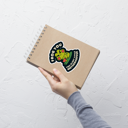 The design features a cartoonish green frog with exaggerated angry features, holding a teacup. The frog has round red cheeks. Above it, text says 'Frog You' and below, 'You Slimy Little Motherhopper'. The style is playful and humorous, reminiscent of cute comic art.