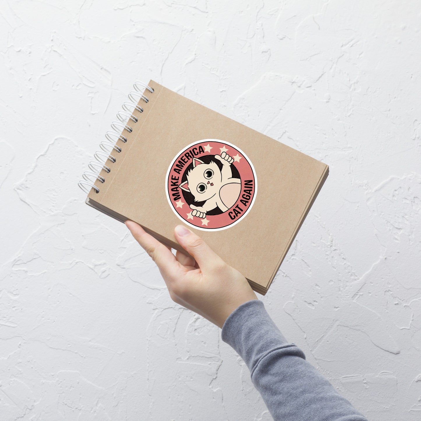 A stamp-style illustration of a cute kitten giving a two-finger thumbs-up, paired with the humorous phrase “Make America Cat Again”. A fun, ironic design for cat lovers and fans of playful pop culture art.