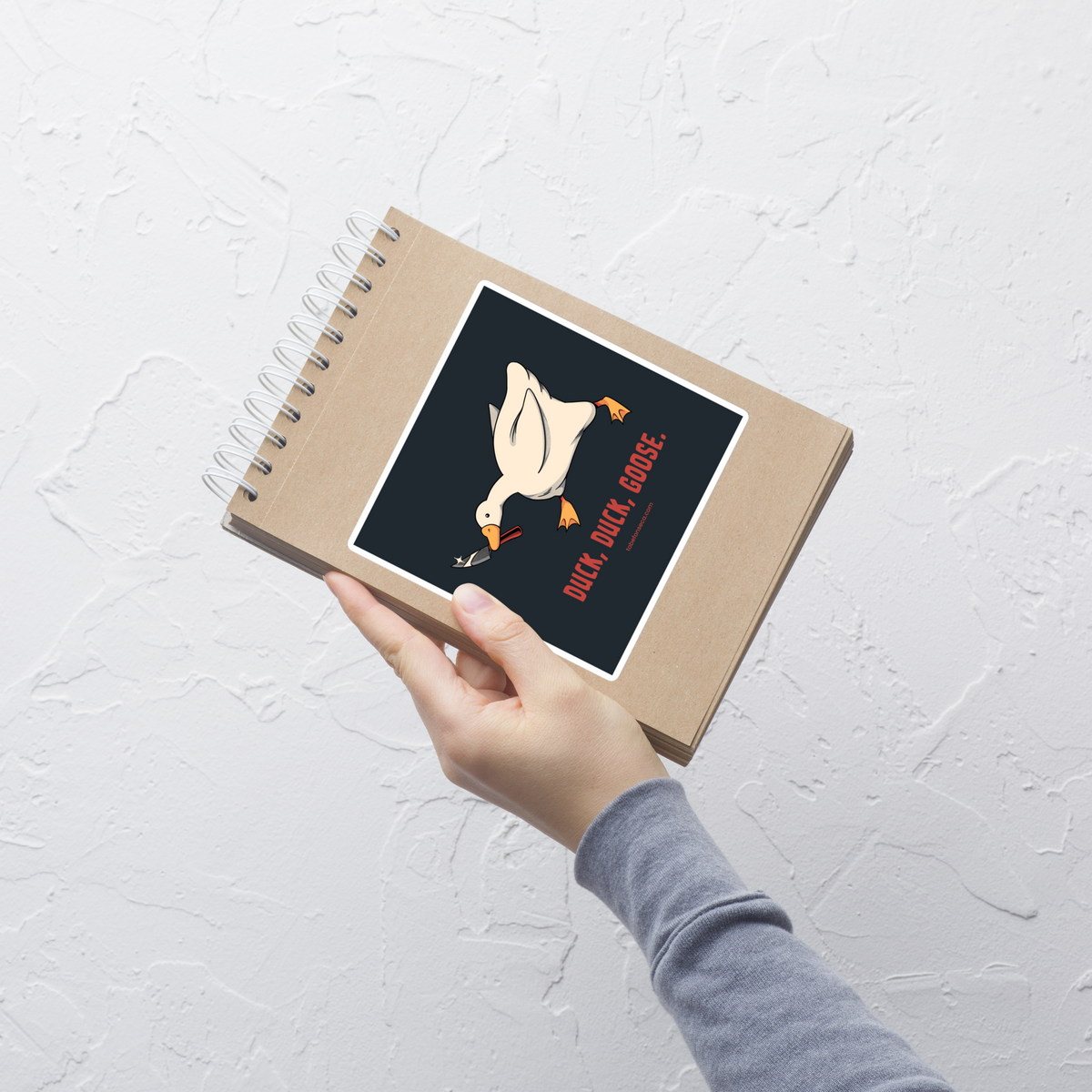 A white goose gripping a sharp knife in its beak with the phrase “Duck, Duck, Goose” below. A playful twist on the classic game, this design captures chaotic goose energy with a sharp dose of dark humor.