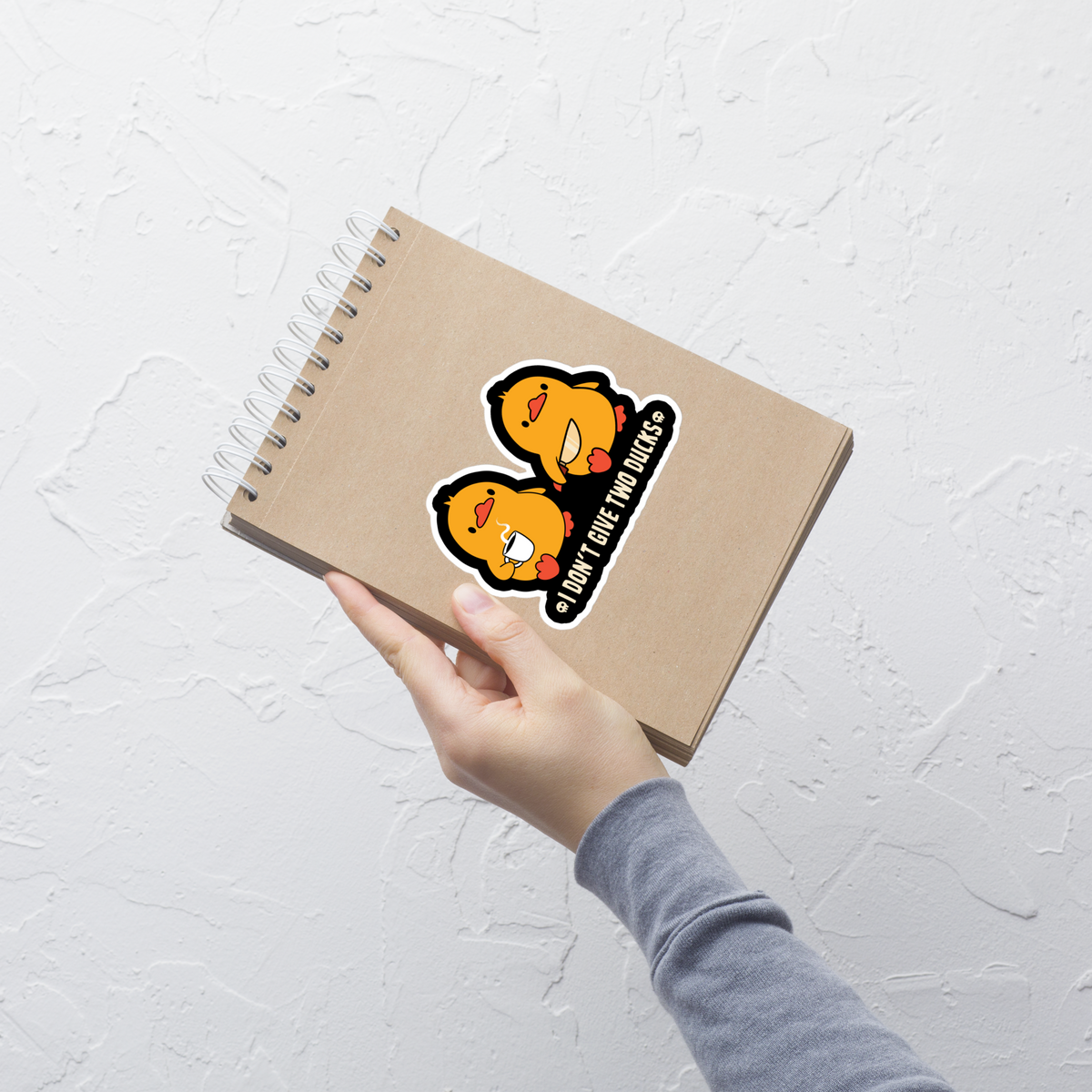 Two cute yellow ducklings, one with a tiny knife and the other holding coffee, alongside the phrase “I Don’t Give Two Ducks”. A playful mix of adorable style and sarcastic humor, perfect for fun t-shirts, stickers and quirky gifts.