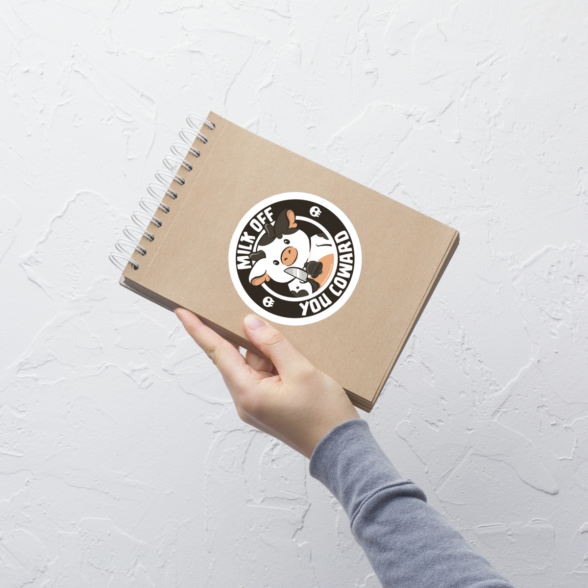 A quirky stamp-style design featuring a cute spotted cow holding a knife alongside the phrase "Milk Off You Coward". Blending dark humour with a cheeky attitude, this playful design is perfect for cow lovers, fans of sarcastic humour, and anyone who enjoys bold, irreverent artwork.