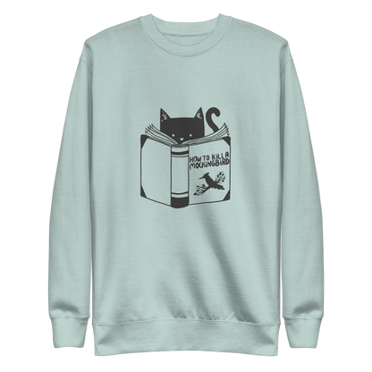 A black and white illustration features a cat peeking over an open book titled 'How to Kill a Mockingbird,' playfully altering the classic novel's title. The cat has a heart-shaped nose and simple, cute facial features. The design is whimsical and ironic, combining classic literature with a humorous twist.