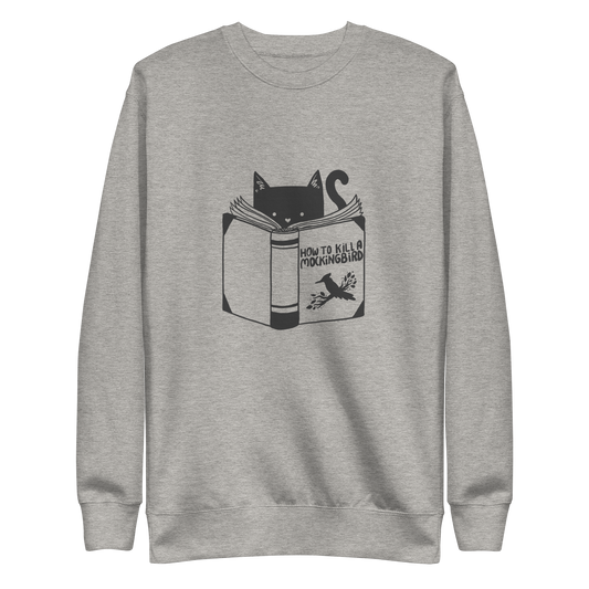 A black and white illustration features a cat peeking over an open book titled 'How to Kill a Mockingbird,' playfully altering the classic novel's title. The cat has a heart-shaped nose and simple, cute facial features. The design is whimsical and ironic, combining classic literature with a humorous twist.