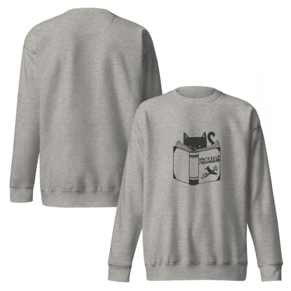 A black and white illustration features a cat peeking over an open book titled 'How to Kill a Mockingbird,' playfully altering the classic novel's title. The cat has a heart-shaped nose and simple, cute facial features. The design is whimsical and ironic, combining classic literature with a humorous twist.