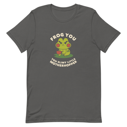 The design features a cartoonish green frog with exaggerated angry features, holding a teacup. The frog has round red cheeks. Above it, text says 'Frog You' and below, 'You Slimy Little Motherhopper'. The style is playful and humorous, reminiscent of cute comic art.