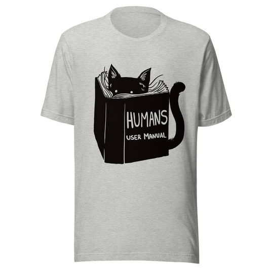 A kitten peeking out from behind a huge book titled "Humans: User Manual". This design plays on the idea that cats are trying to figure out how to control us. Perfect for cat lovers, book fans, and anyone who enjoys lighthearted humor in prints.