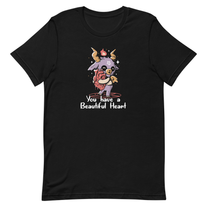 The design features a cute, cartoonish, anthropomorphic goat with big horns and a flame above its head, standing on a red pentagram. The goat has a star on its forehead and is hugging a large, anatomically correct human heart. The text below reads, 'You have a Beautiful Heart'. The image combines elements of occult symbolism with a playful, endearing aesthetic.